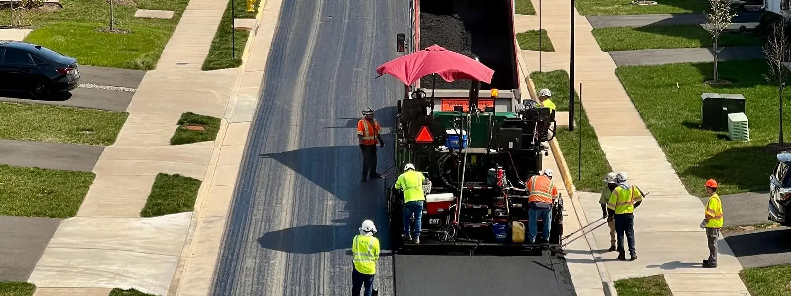 Asphalt paver laying a fresh mat down a residential street, with the milled surface ahead of it