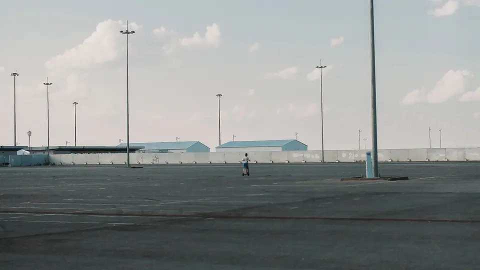 Wide empty asphalt parking lot with light poles under an open sky