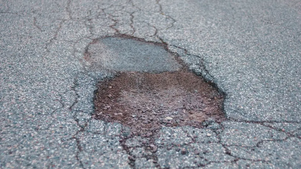 Asphalt surface where an old patch has failed and cracking has spread out around it